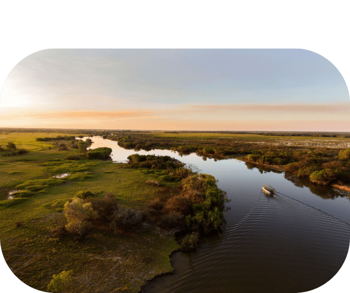 Aerial view of a boat on a river winding through green fields at sunset.
