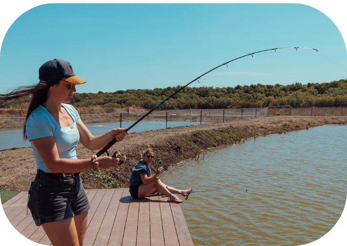 Two people fishing on a dock by a pond under a clear blue sky.